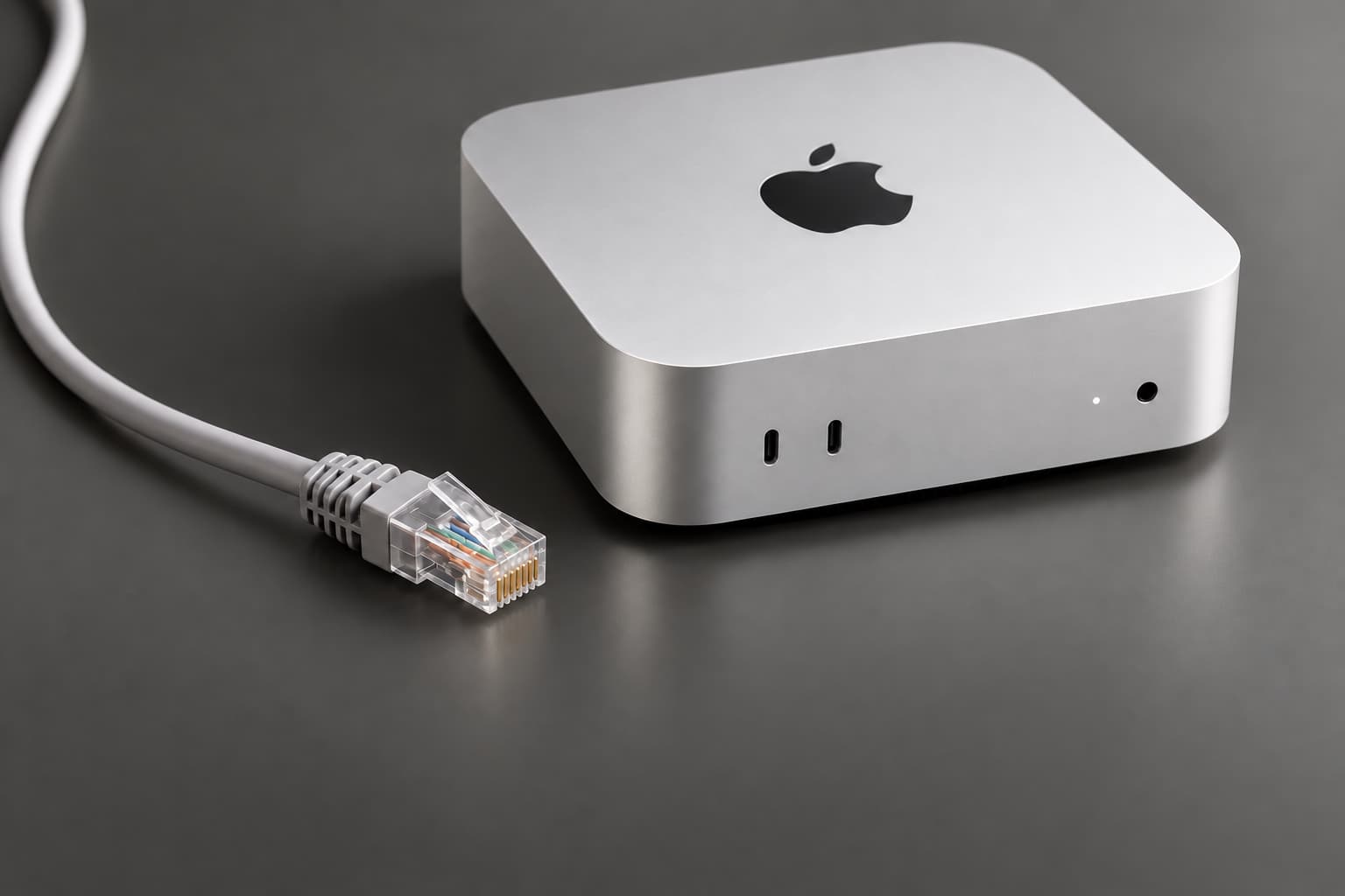 A silver Mac mini and an Ethernet connector on a smooth graphite background